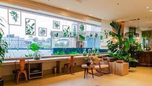A modern interior with a seating area by a large window, featuring framed plant art and various potted plants. - Ibis Styles Curitiba Airport Hotel (Sao Jose dos Pinhais)