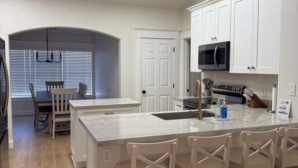 A modern kitchen with white cabinetry, a central island with bar stools, a microwave, and a sink. - Newly Remodeled Mesa Oasis with a Sparkling Pool—Move-In Ready & Stunning! (Mesa)