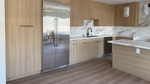 A modern kitchen with wooden cabinets, a stainless steel refrigerator, a marble backsplash, and a black faucet.