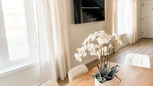 A modern dining area with a wooden table, white chairs, and a vase of white orchids.