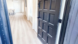 A hallway with a dark wooden door, white curtains, and a light wooden floor.