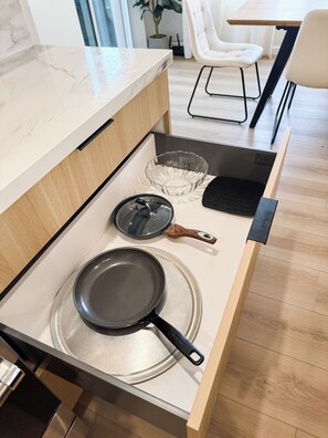 Un tiroir de cuisine contenant une poêle, un saladier en verre et une spatule noire.