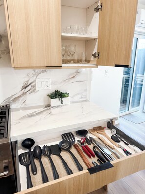 Une cuisine dotée d’un plan de travail en marbre, de meubles de rangement en bois et d’un tiroir contenant des ustensiles de cuisine.