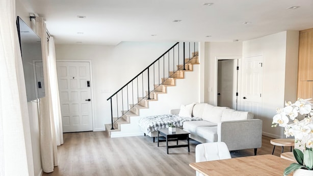 A spacious living area with a wooden floor, a staircase, and a dining area with white chairs and a wooden table.
