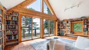 Een ruime kamer met grote ramen, houten boekenkasten, een witte bank en uitzicht op de omgeving.