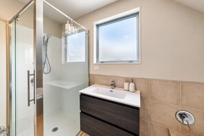 Ein modernes Badezimmer mit Duschkabine aus Glas, Waschtisch und einem Fenster über dem Spiegel.