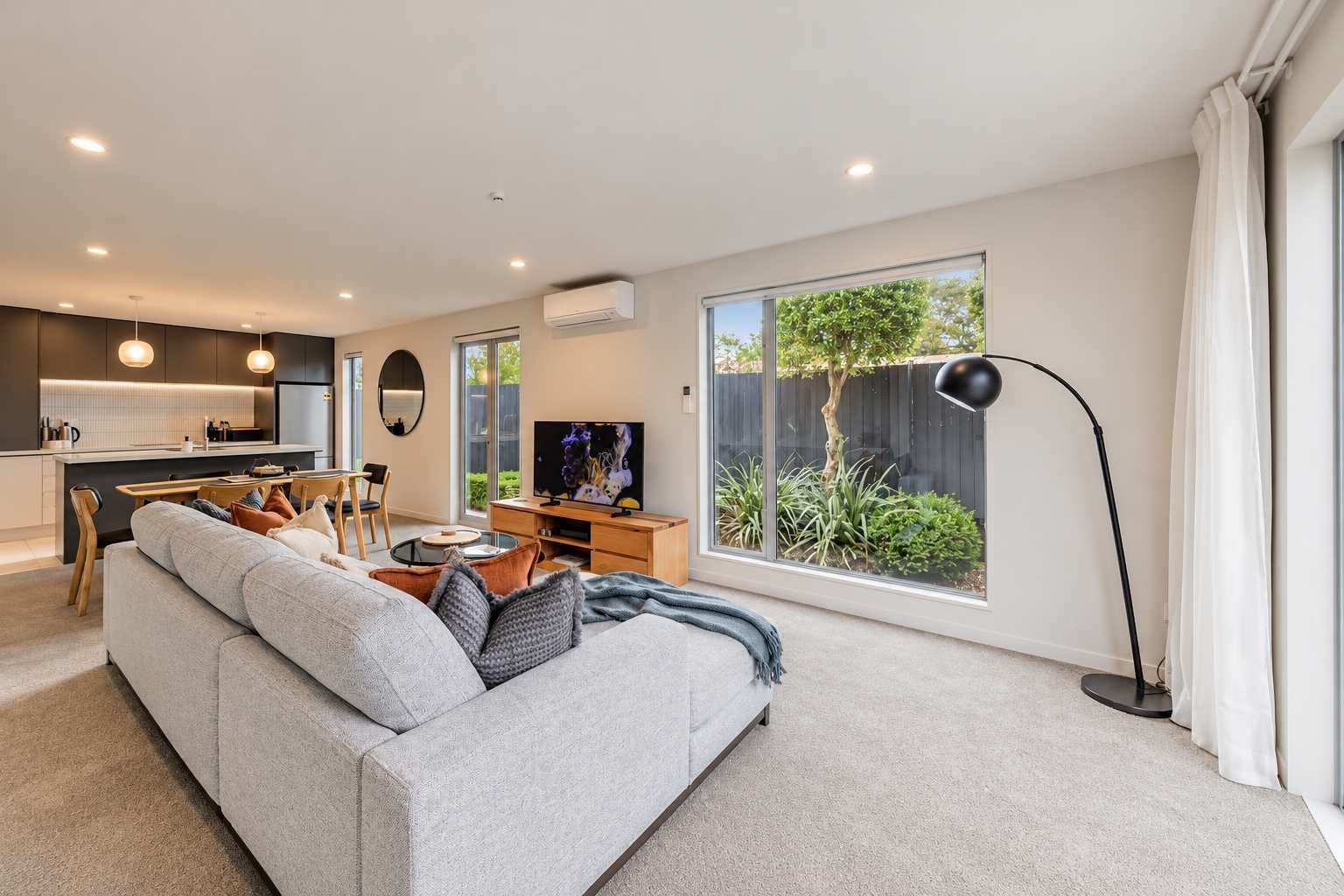 A modern living room with a grey sofa, a dining area, and a kitchen in the background.
