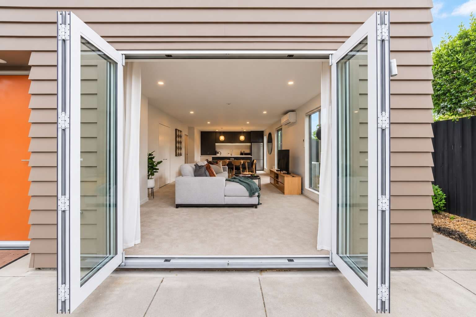 Un interior moderno de vivienda con sala de estar, cocina y comedor visibles a través de una puerta corrediza de vidrio.