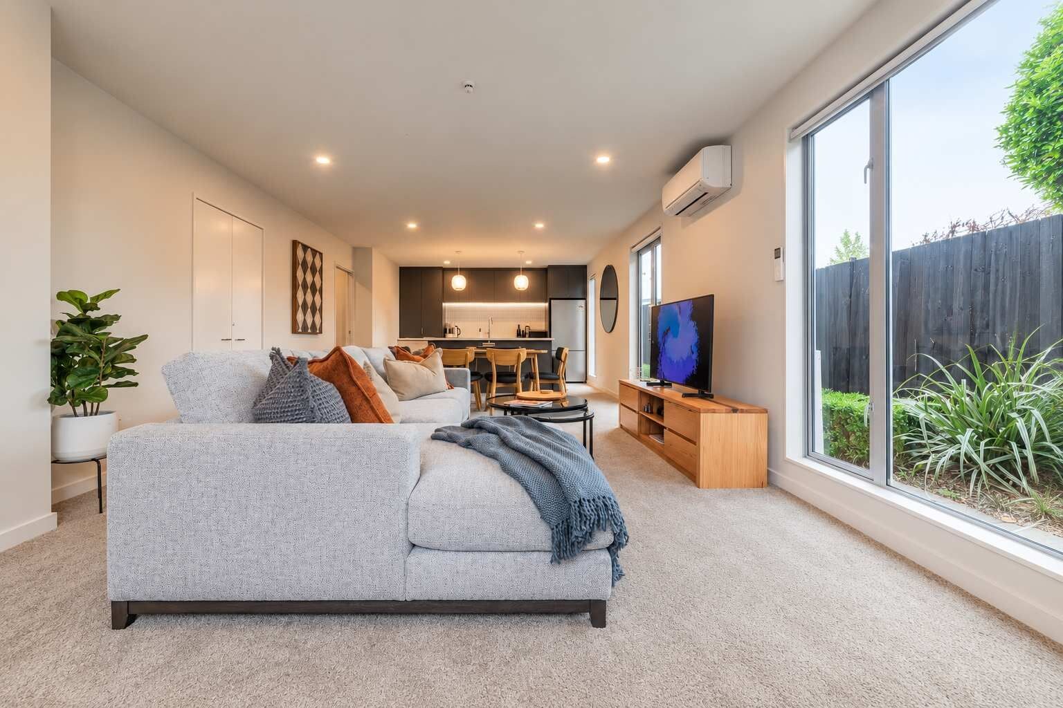 A modern living room with a grey sofa, a flat-screen TV, and a large window.
