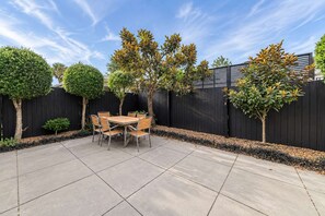 Eine Terrasse mit Tisch und Stühlen, umgeben von einem schwarzen Zaun und Bäumen.