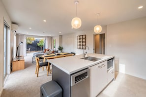 A modern kitchen with a central island, a dining area with a table and chairs, and a view of the outdoors through large windows. - Central Richmond | Modern 3BR + Courtyard (Christchurch)