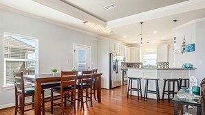A modern kitchen with wooden flooring, white cabinets, a central island with bar stools, and a dining area with a wooden table and chairs. - Blissful Waves - Pet Friendly, Walk to the Beach! (Bolivar Peninsula)