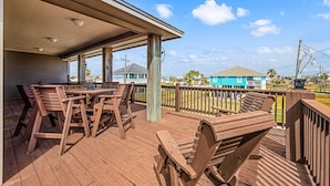A wooden deck with tables and chairs, overlooking a residential area with houses and a clear sky. - Blissful Waves - Pet Friendly, Walk to the Beach! (Bolivar Peninsula)