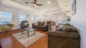 A spacious living room with a brown leather sofa, a green rattan chair, and a glass coffee table. - Blissful Waves - Pet Friendly, Walk to the Beach! (Bolivar Peninsula)
