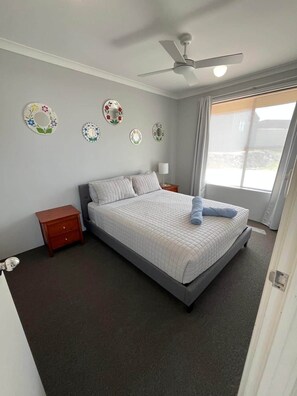 Un dormitorio con cama, mesita de noche, ventilador de techo y espejos decorativos en la pared.