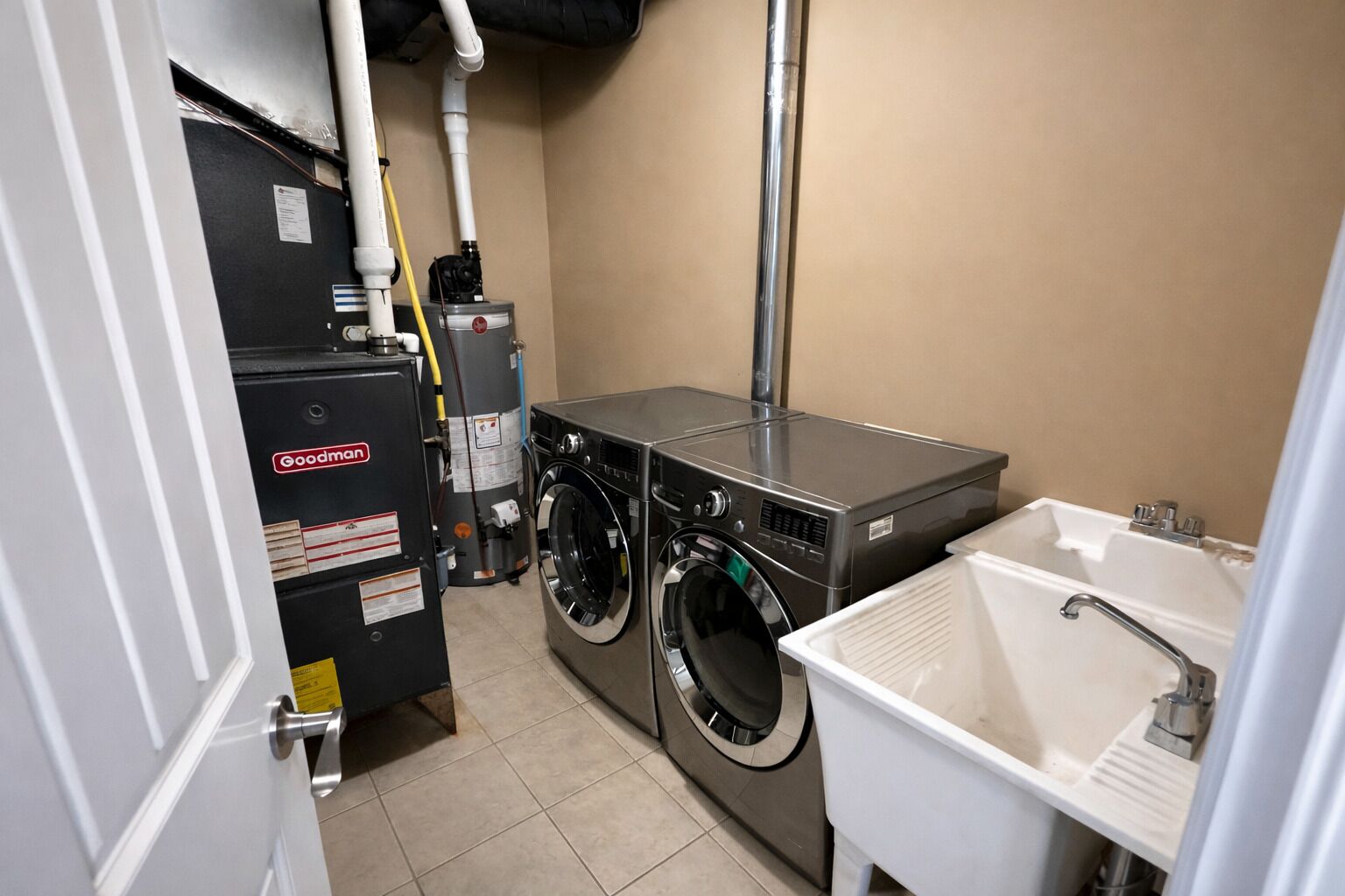 Une buanderie équipée d’un lave-linge et d’un sèche-linge à chargement frontal, d’un évier et d’un chauffe-eau.
