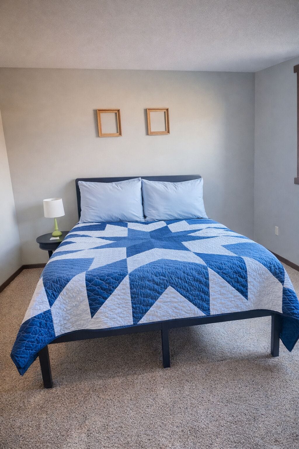 Uma cama com um edredom azul e branco, um abajur e duas molduras na parede.
