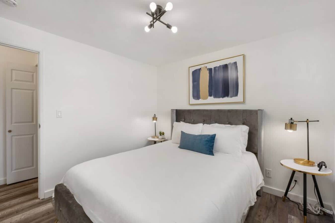 Une chambre à coucher avec un grand lit, une table de chevet avec une lampe, une petite table avec une lampe et un tableau au mur.