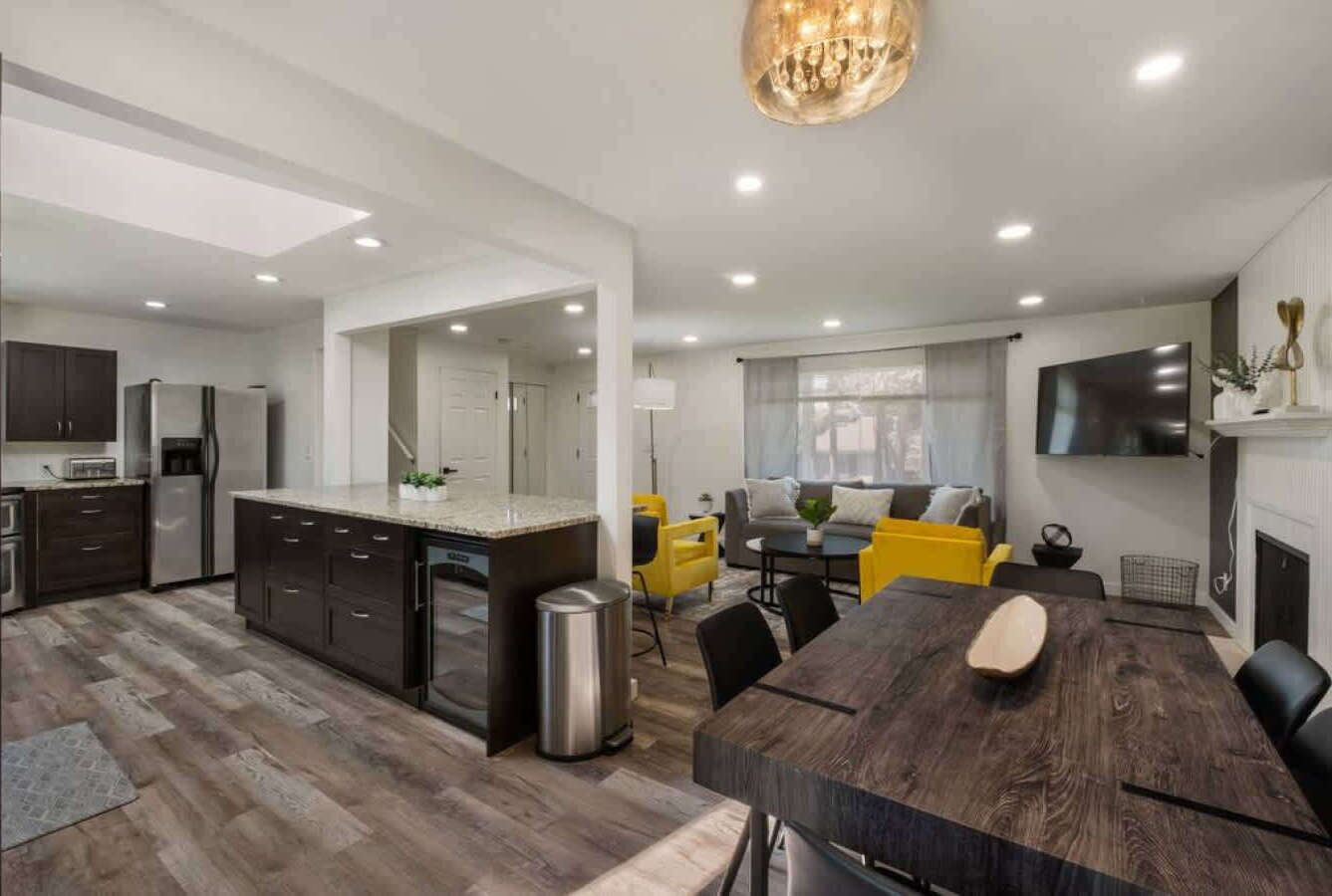Une cuisine moderne avec des meubles de couleur sombre, un îlot central et un coin repas comprenant une table et des chaises en bois.