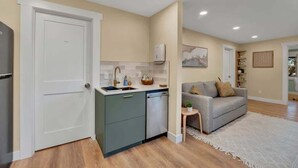 A compact living space with a kitchenette, a grey sofa, and a small side table. - Westlake Nest | Minutes to DT | Quiet & Renovated! (Seattle)