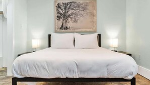 Une chambre à coucher avec un grand lit, deux tables de chevet avec des lampes et un tableau représentant un arbre au mur.