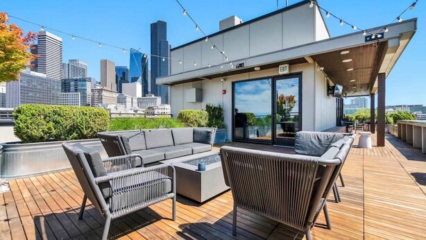 Eine Dachterrasse mit einem modernen Außenbereich zum Sitzen, inklusive Sofa und Sesseln, mit Blick auf die Stadtlandschaft.
