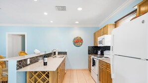Una cocina con armarios de madera, un refrigerador blanco, un microondas y una botella de vino sobre la encimera.