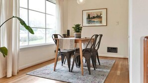 A dining area with a table, chairs, a potted plant, a painting, and a window with curtains. - Mellow Yellow | UW & Children's | Backyard Patio! (Seattle)