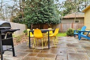 Een terras met een tafel, stoelen, een barbecue en een houten omheining op de achtergrond.