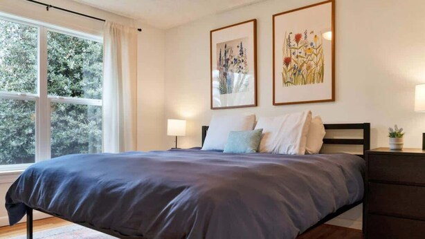 A bedroom with a large bed, a nightstand, a dresser, and two framed floral paintings on the wall. - Mellow Yellow | UW & Children's | Backyard Patio! (Seattle)