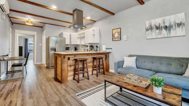 A modern kitchen with wooden beams, a central island with stools, a grey sofa, and a painting on the wall. - New! Prime DT Modern - Extended stay Equipped! (Tacoma)