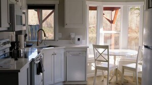 Une cuisine moderne avec des meubles blancs, un lave-vaisselle et un coin repas comprenant une table et des chaises blanches.