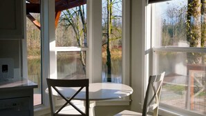Une pièce d’angle avec une baie vitrée, une table à manger avec des chaises, et une vue sur des arbres et un jardin.