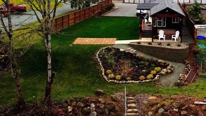 Un jardin bien entretenu, agrémenté d’un chemin en pierre, d’un petit espace aménagé pour s’asseoir et d’une terrasse en bois.
