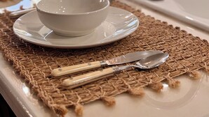 A kitchen counter with a white bowl and plate on a woven placemat, a knife, and a spoon.