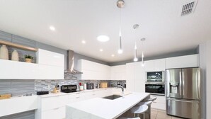 Een moderne keuken met witte kastjes, een marmeren eiland, roestvrijstalen apparatuur en hanglampen.