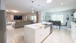 Een moderne keuken met een centraal eiland, een eethoek met tafel en stoelen, en een zithoek met bank en televisie.