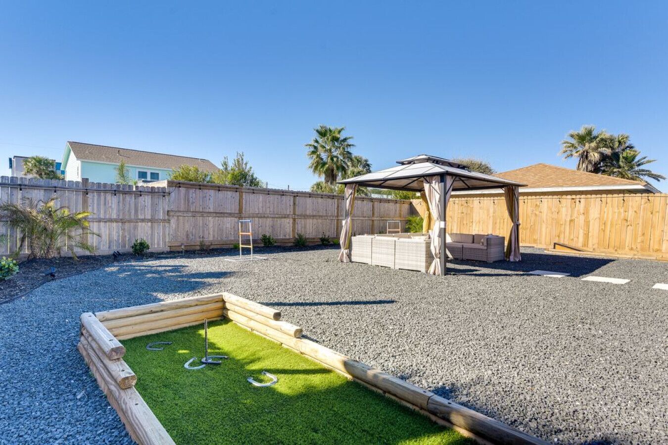 A backyard with a wooden fence, a pergola, a sandbox, and a small grassy area.