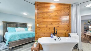 Un dormitorio con cama, pared de madera, bañera y baño con silla y estante.