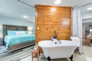 A bedroom with a bed, a wooden wall, a bathtub, and a bathroom with a chair and a shelf. - Sleeps 20 | 3 Miles to Beach | Fire Pit & BBQ (Galveston)