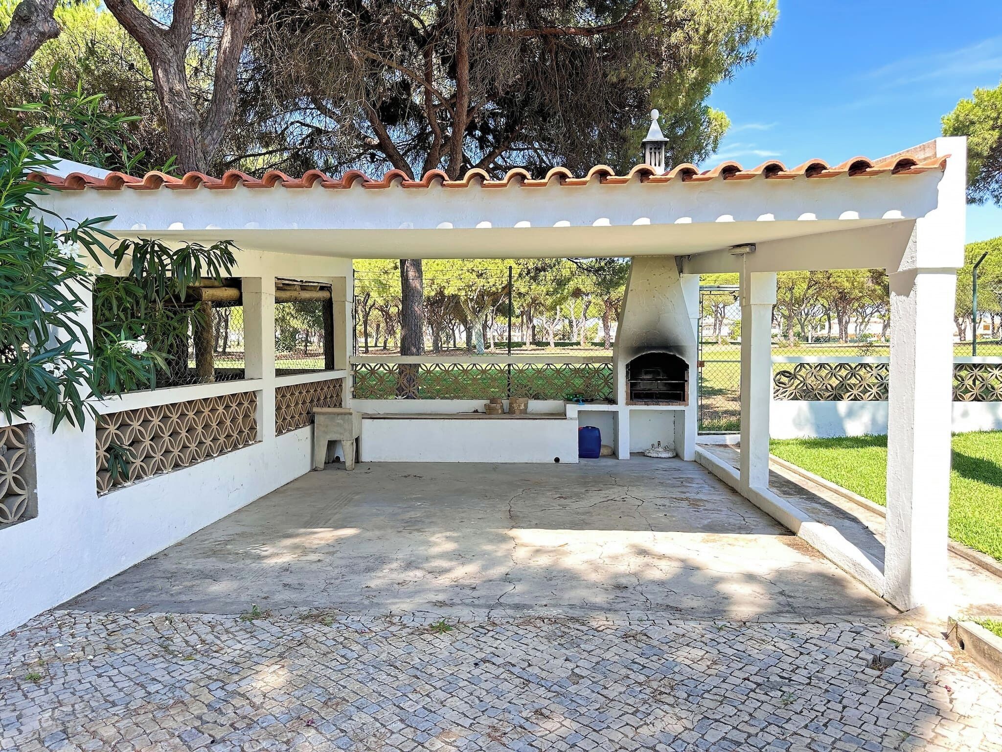 An outdoor patio with a tiled floor, a white pergola, and a brick oven.