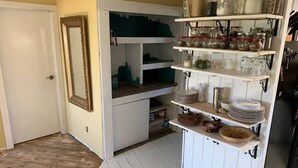 A kitchen with white cabinets, a wooden floor, and shelves with jars and plates. - Dome house in Centennial valley (Laramie)