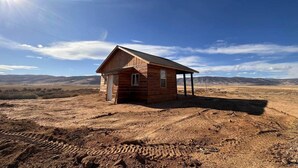 Eine kleine Holzhütte mit einem einzigen Fenster und einer Tür, eingebettet in eine offene, trockene Landschaft.