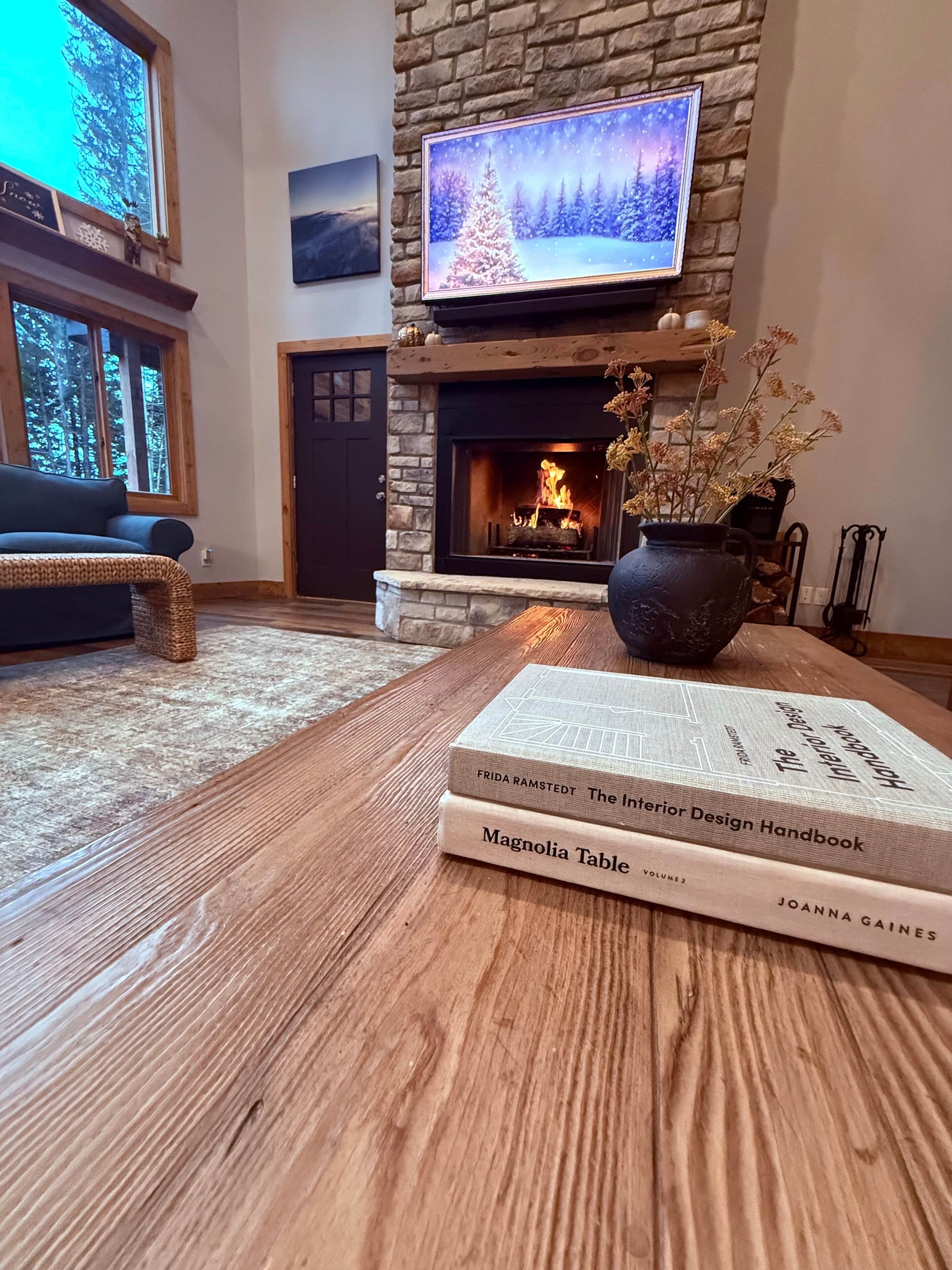 A cozy living room with a fireplace, a television mounted above it, and a table with books.