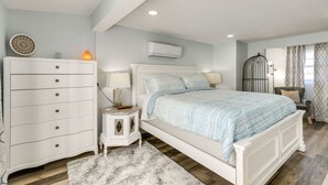 A bedroom with a bed, dresser, nightstand, and a window with curtains. - Galveston Beach Retreat | Balcony & Walk to Seawall (Galveston)