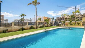 A swimming pool with a clear blue water, surrounded by a well-maintained lawn and palm trees. - Modern 1BR Flat with pool, 1 min from Torrox’s Beach (Nerja)