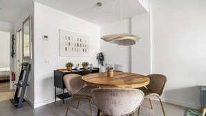 A modern dining area with a round wooden table, two upholstered chairs, and a pendant light. - Modern 1BR Flat with pool, 1 min from Torrox’s Beach (Nerja)