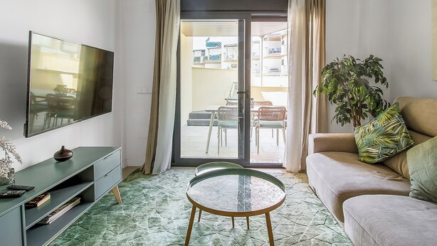 A living room with a flat-screen TV, a glass table, a sofa, and a sliding glass door to an outdoor area. - Modern 1BR Flat with pool, 1 min from Torrox’s Beach (Nerja)