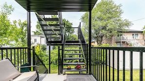 A covered outdoor area with a metal staircase leading to a higher level, a bench, and toys on a table. - 10-Min La Ronde Ride! Cozy Place, Free Parking! (Longueuil)
