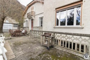 Ein Gebäude mit einem Balkon, einem Essbereich mit Stühlen und einem Tisch sowie einem Fenster mit Blick auf Bäume.